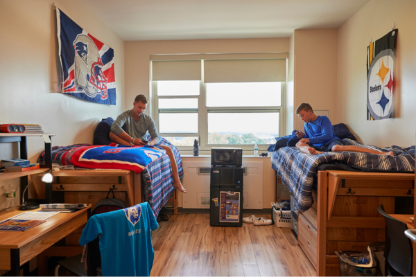two male students, each sitting on their residence hall bed talking to each other