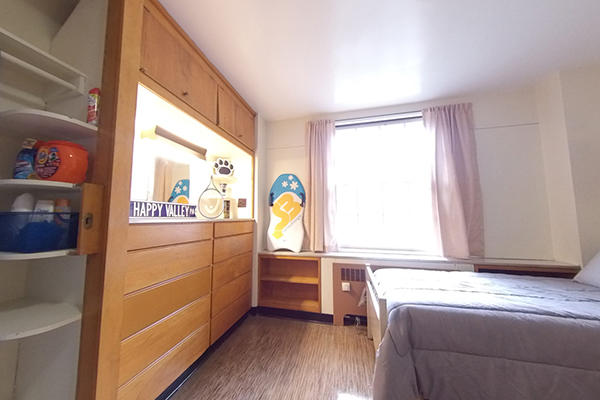 A well-organized dorm room with wooden furniture, storage, and a bed.