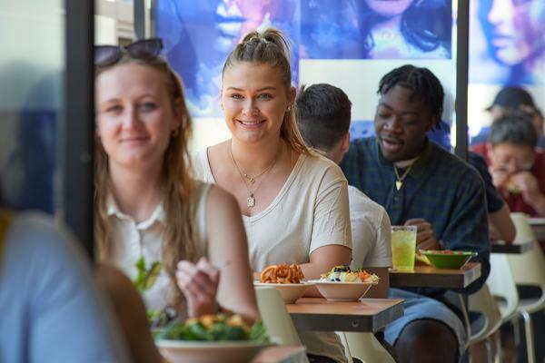 students sitting at tables in dining hall eating a meal