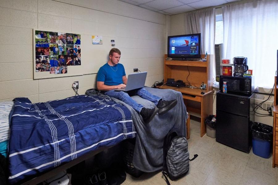 Male student sitting on bed in residence hall room