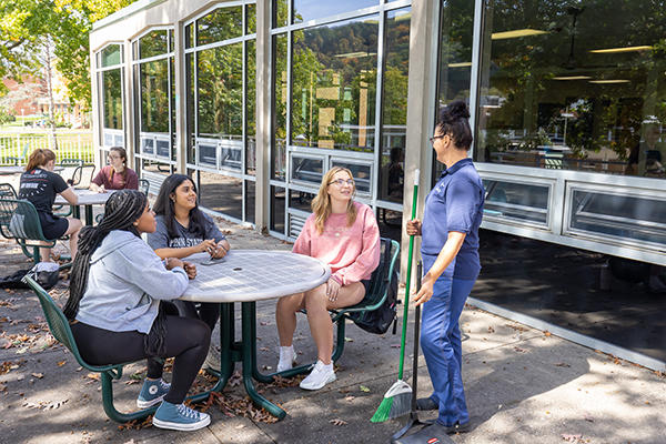Students visit with employee on Oak Hall's patio