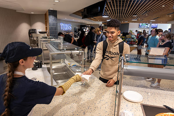 Student employee hands sandwich to customer