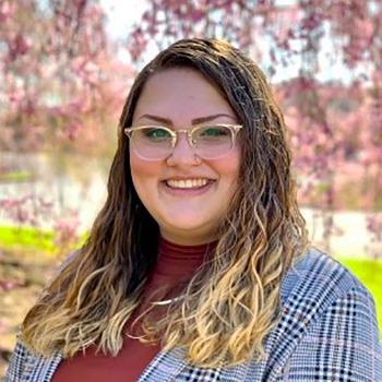 Staff_CL_(Welch B)_700x700_2021 A smiling Bailey Welch outside in front of a flowering tree