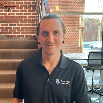 A smiling Kyle Kowal standing in front of a staircase in the Woods Complex