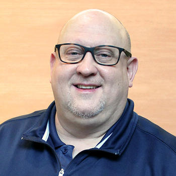 A smiling Craig Cook in front of a pale wood background