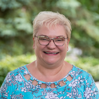 A smiling Gina Greppin among trees and sunlight