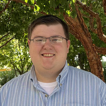 A smiling Nate Dealy in front of a tree outside Stacks