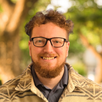 A smiling Austin Towner against a backdrop of trees and sunlight