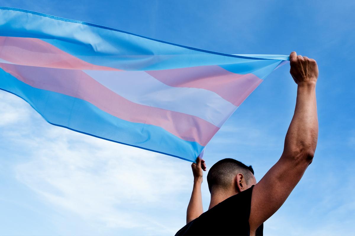 Gender Neutral Housing Man holding a pink, blue and white flag