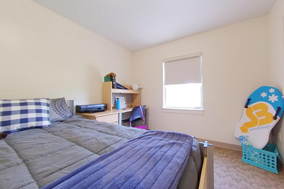 A tidy dorm room with a bed and wooden furniture.