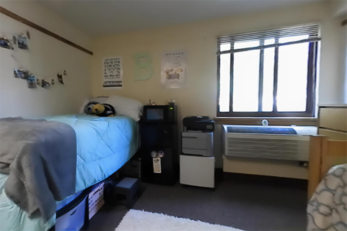 A tidy dorm room with a bed and wooden furniture.