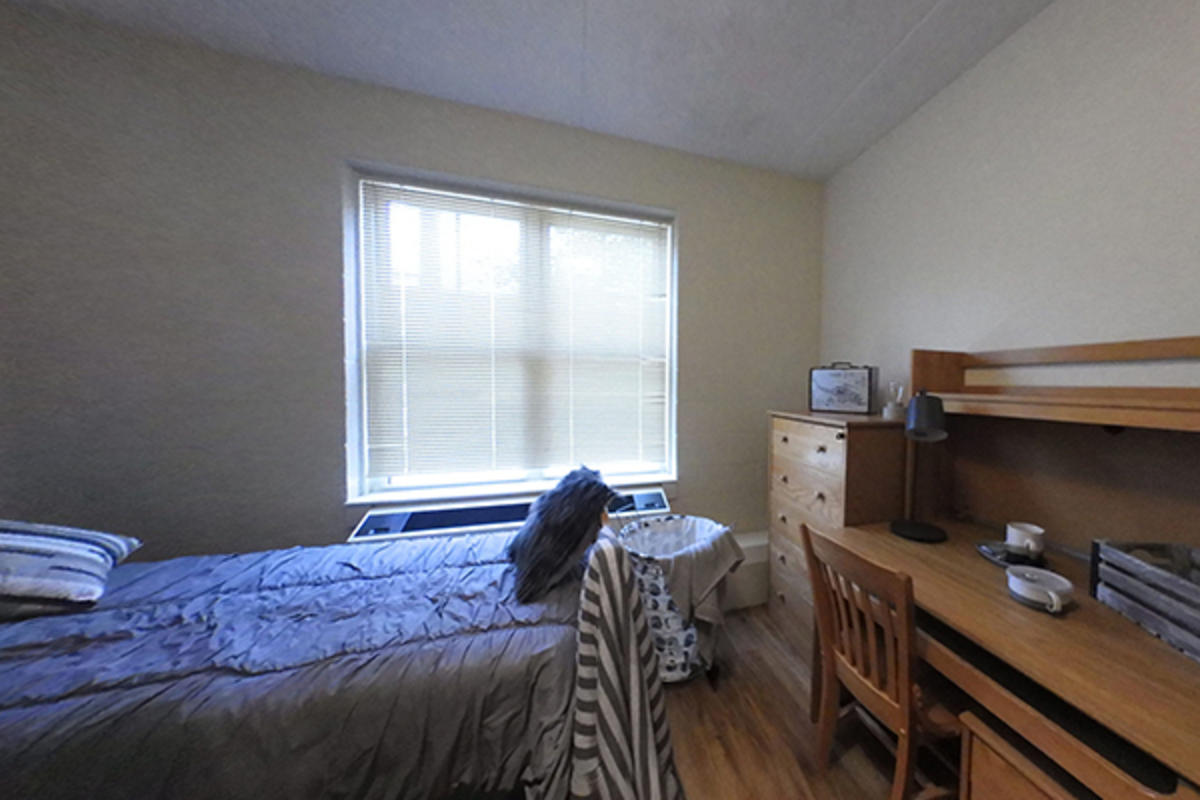 A tidy dorm room with a bed and wooden furniture.