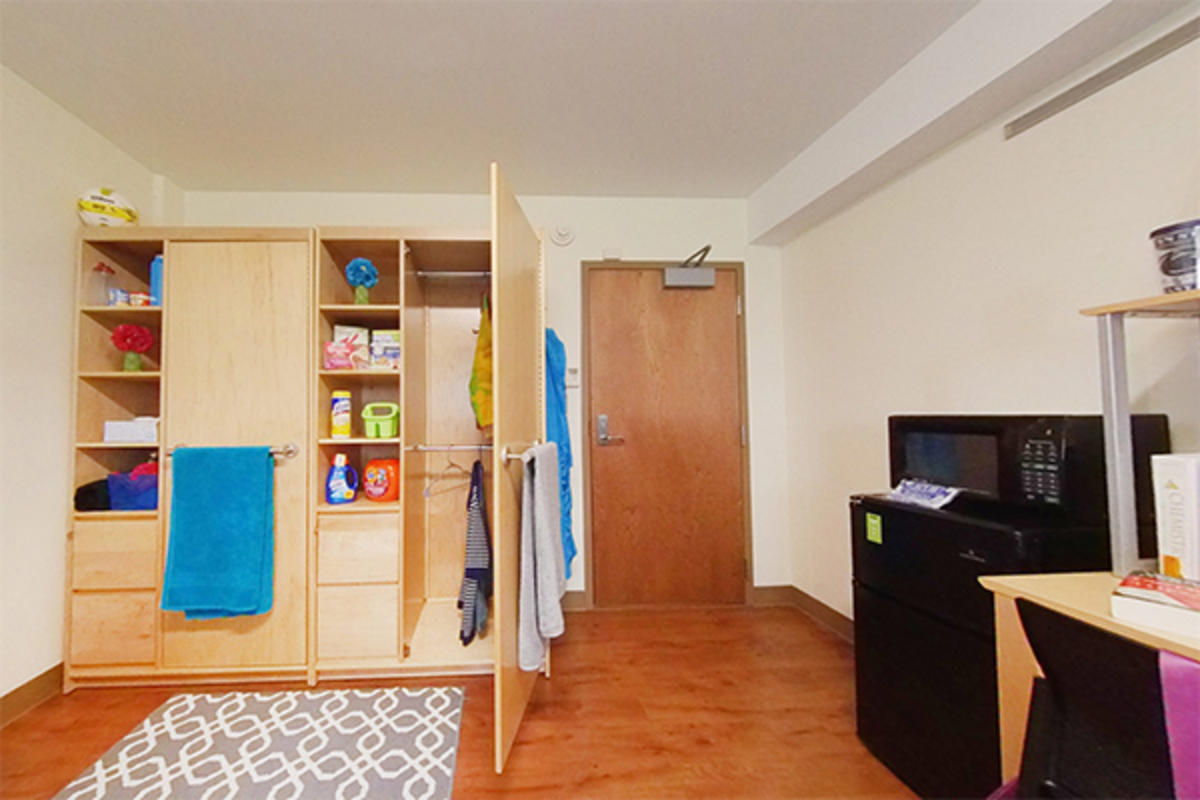 A well-organized dorm room with wooden furniture and storage.