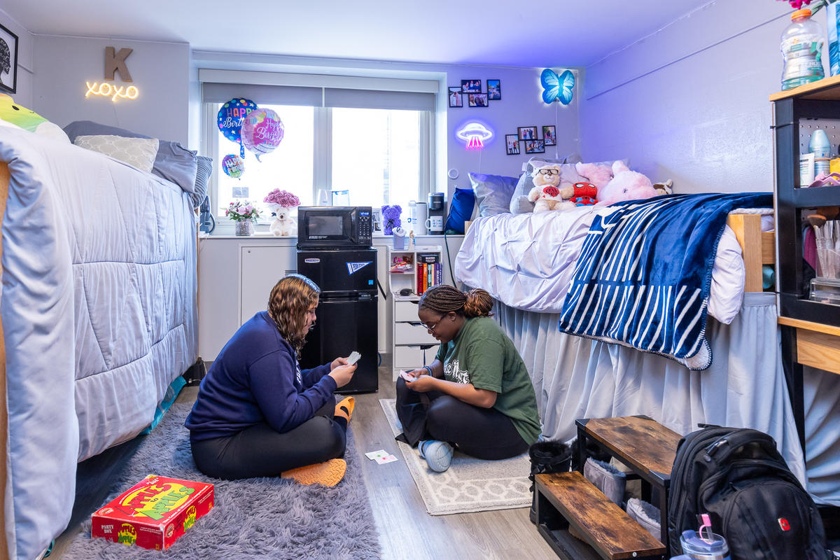 Geary residence hall room with two students sitting on the floor playing a game.