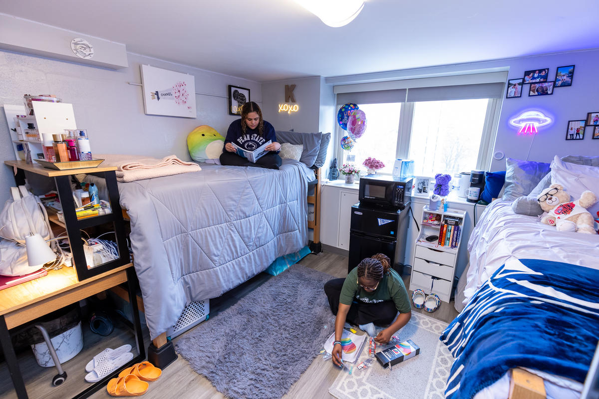 Geary residence hall room with a student studying on their bed to the left and a student working on crafts on the floor to the right.