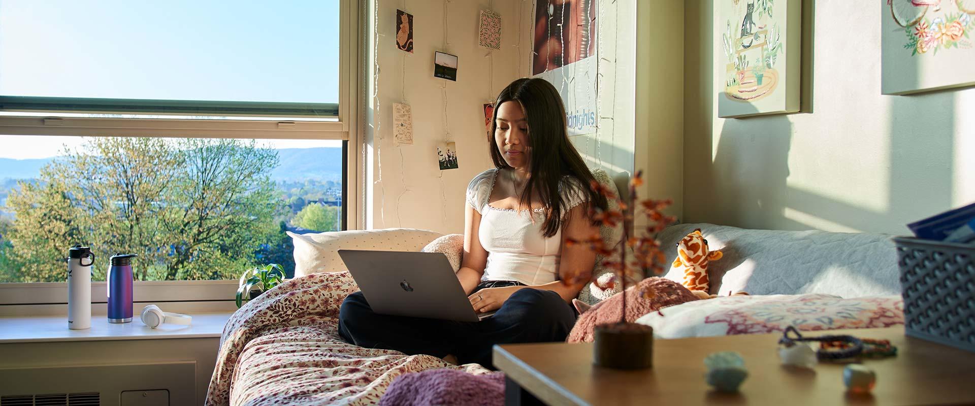 college student sitting on bed in residence hall room