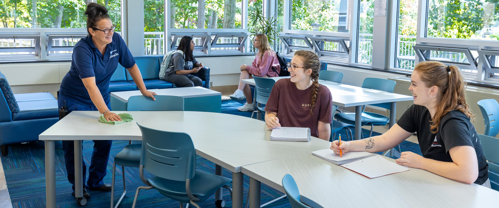 Housing Services Employee cleans desk surfaces while chatting with students